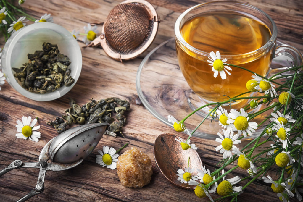 A clear cup of chamomile tea lays on the table next to loose tea and flowers from the traditional Arabic tea culture that you can visit with Jaya Travel.