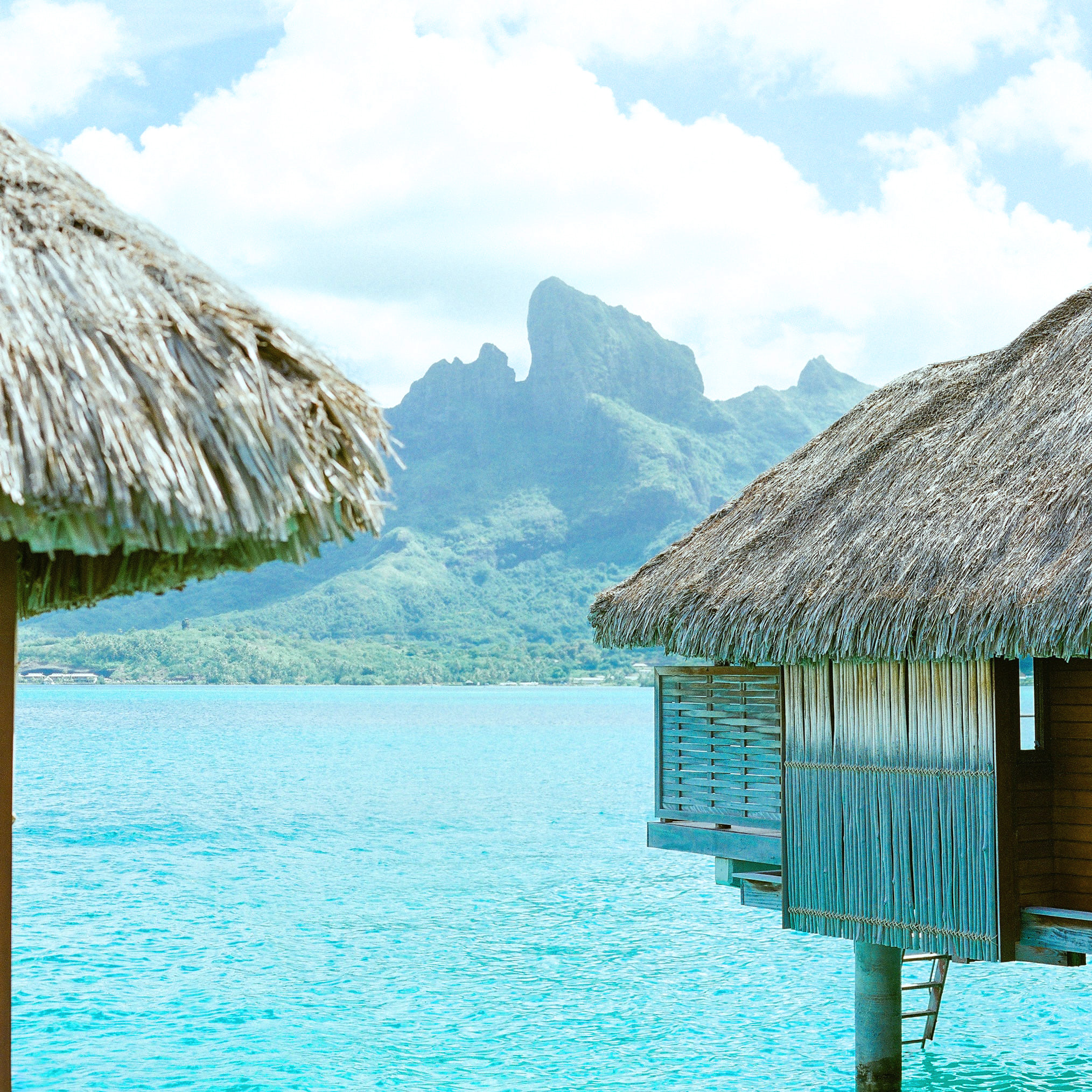 Luxury overwater bungalow hotels at Tahiti resort in Bora Bora, French Polynesia travel with the beach and mountains in the background.