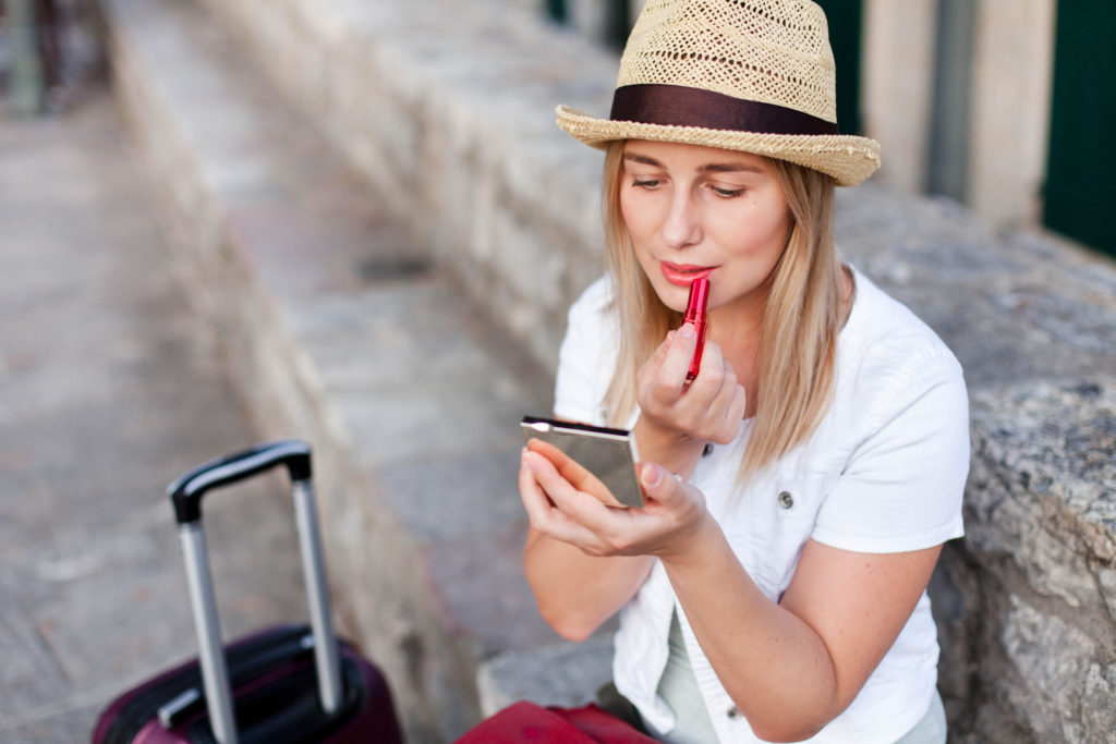 a woman re-applies lipstick while on travel and tours with Jaya, where she uses our traveling with makeup tips.