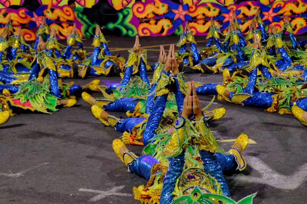 dancers wearing bright culture outfits with blue, yellow, and green sparkles and feathers lay on the ground performing a traditional dance for the must see festivals of Aliwan where tourists can celebrate the traditional way with Jaya.