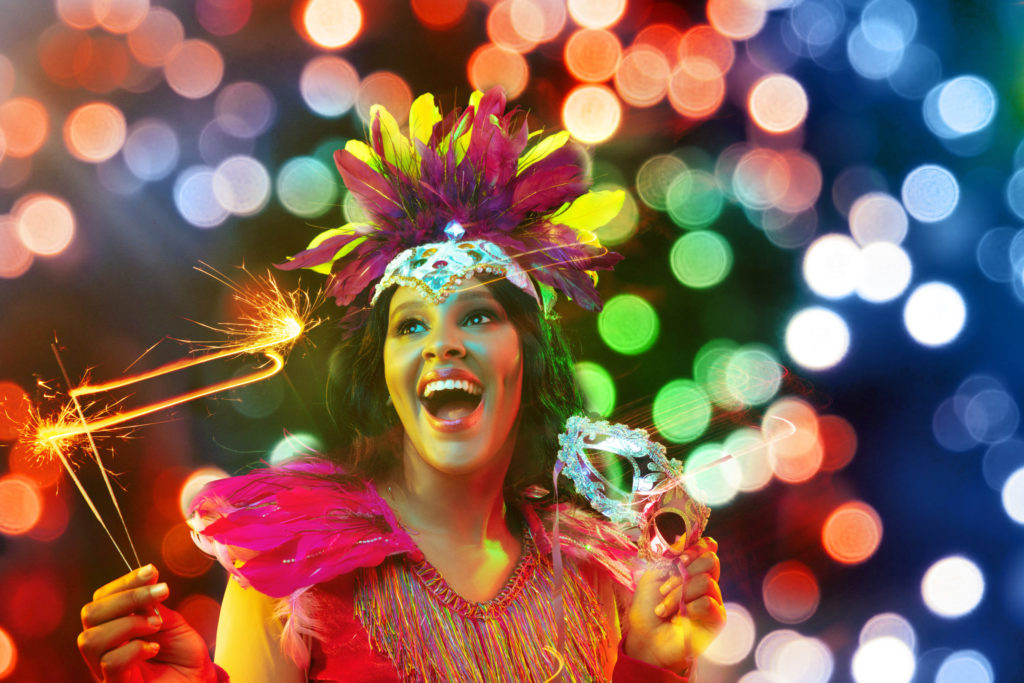 a beautiful woman wears a tradition masquerade mask and colorful costume to celebrate the must see festival carnival where people dress in bright colors, embrace cultural traditions, and have fun with Jaya Travel and Tours.