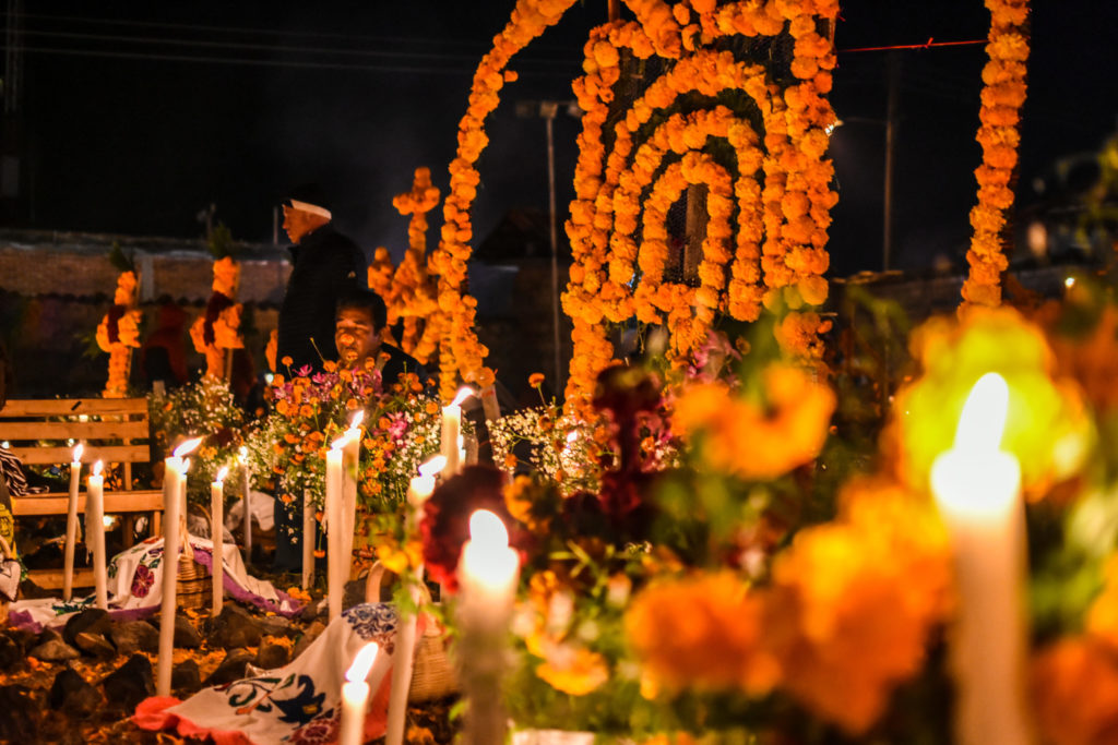 A Dia De Los Muertos celebration of tradition and culture taking place in a traditions graveyard with marigolds, food, and music, to celebrate the unique festival with Jaya Travel.