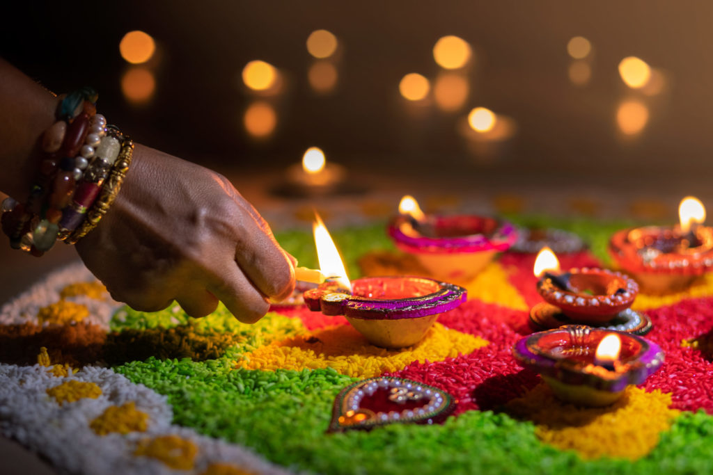 an indian woman reaches her hand out to light a tradition culture diwali lamp for the unique celebration and culture experience with Jaya on tour at the must see festivals of Diwali.