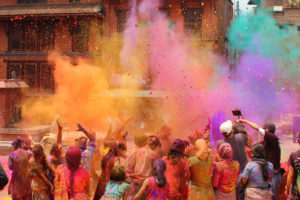 a large group throws colorful powder in the air and at each other for the unique celebration and traditions of Holi by travel with Jaya Travel & Tours at this must see festival.