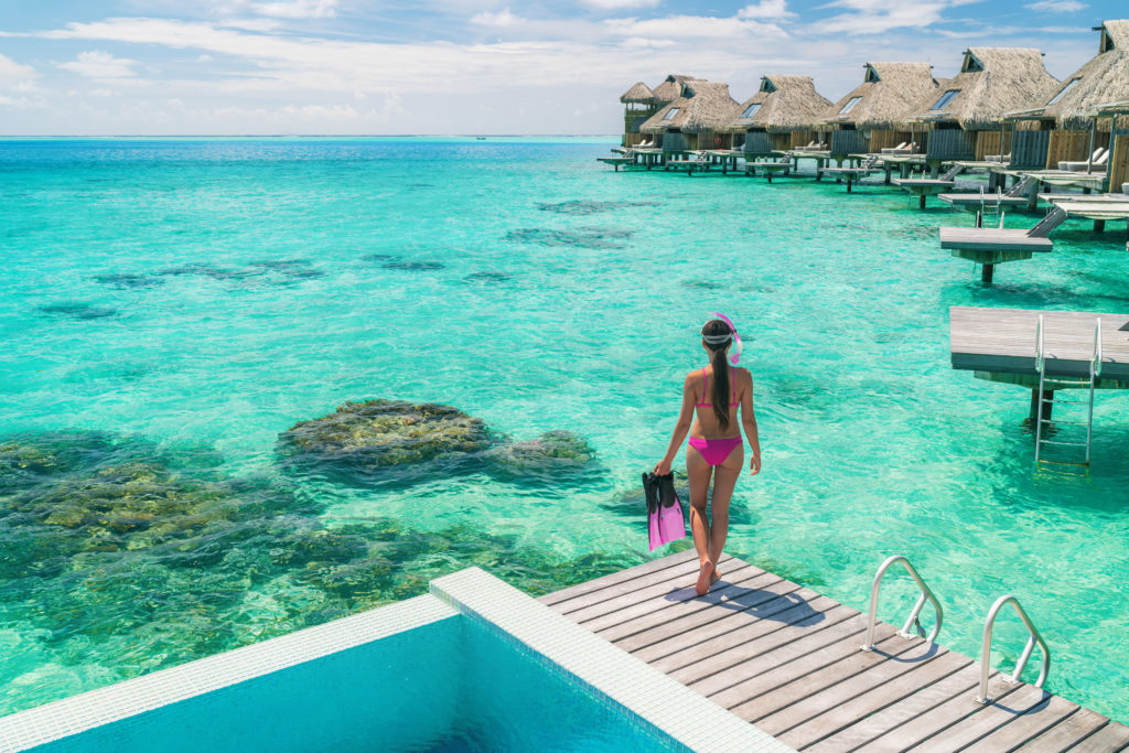 Luxury overwater bungalows at Tahiti resort in Bora Bora, French Polynesia where a woman is going to do leisure watersport recreational activities from a private hotel room on the island vacation.