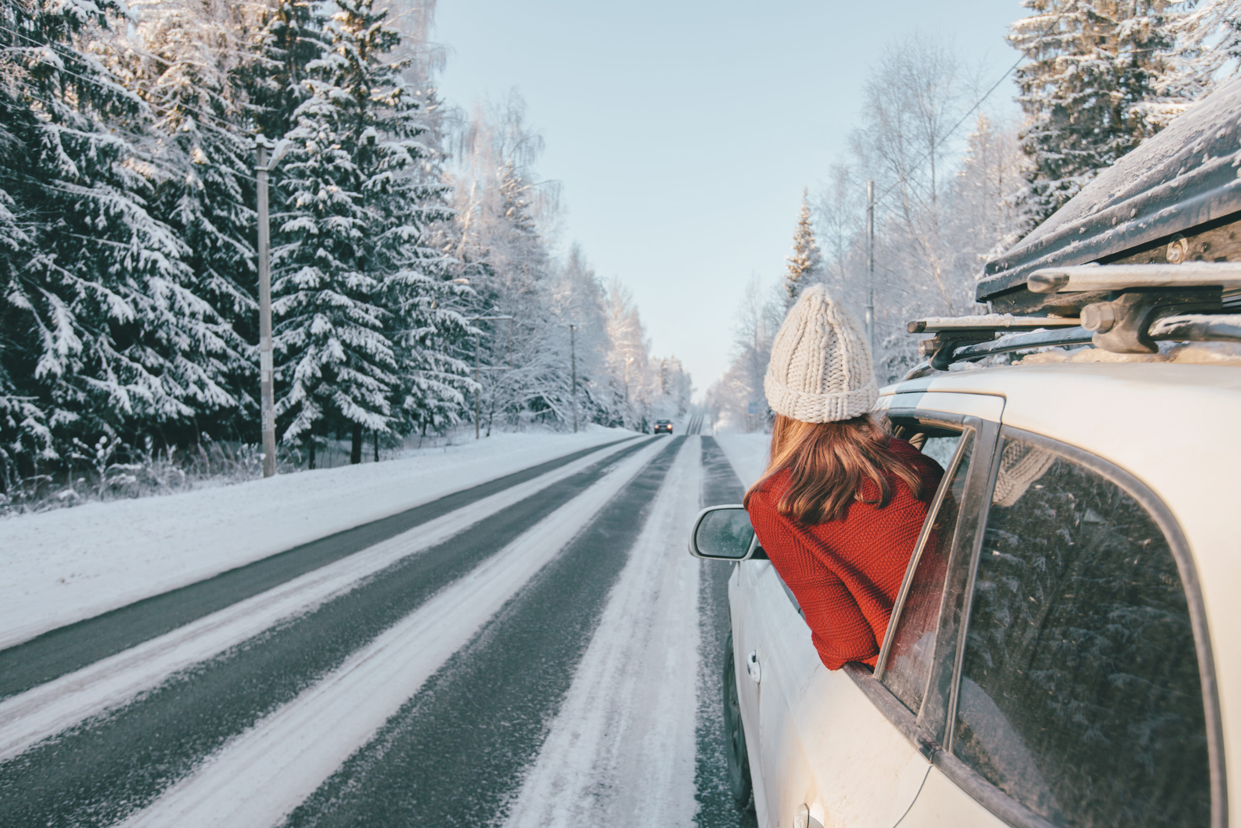 A woman looking out the car window at a scenic winter highway through a forest with snow.