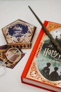 Assorted Harry Potter merchandise of round glasses, chocolate frogs, a magic wand, and a book that were bought from vacation, travel, and tour.