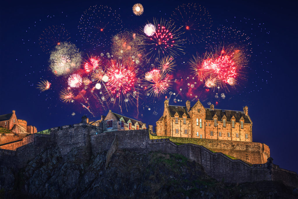 the castle of edinburh with bright fireworks exploding around it as a new year's eve celebration party for the new year that you can tour with Jaya Travel & Tours.