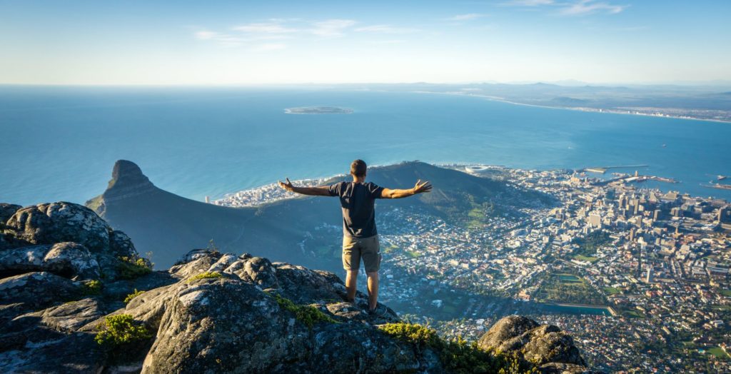 A man climbed to the top of a mountain in Cape Town, South Africa where he is looking over the beautiful city below which was the film location of the movie Invictus.