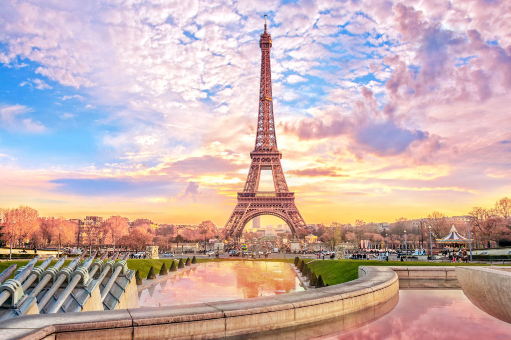 The tourist spot Eiffel Tower stands tall in front of a sunset in Paris, France against a romantic travel tours vacation background.