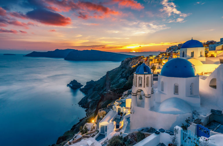 A seaside beautiful view of the white buildings with blue domed roofs while on vacation in Oia village, Santorini island in Greece, a beautiful spot for travel and tours of the Mediterranean.