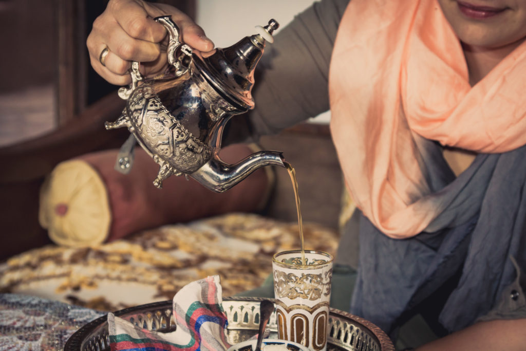 a woman holds a traditional lybian tea pot and pours tea into a cup for guests to enjoy a cup of traditional arabic tea on travel with Jaya.