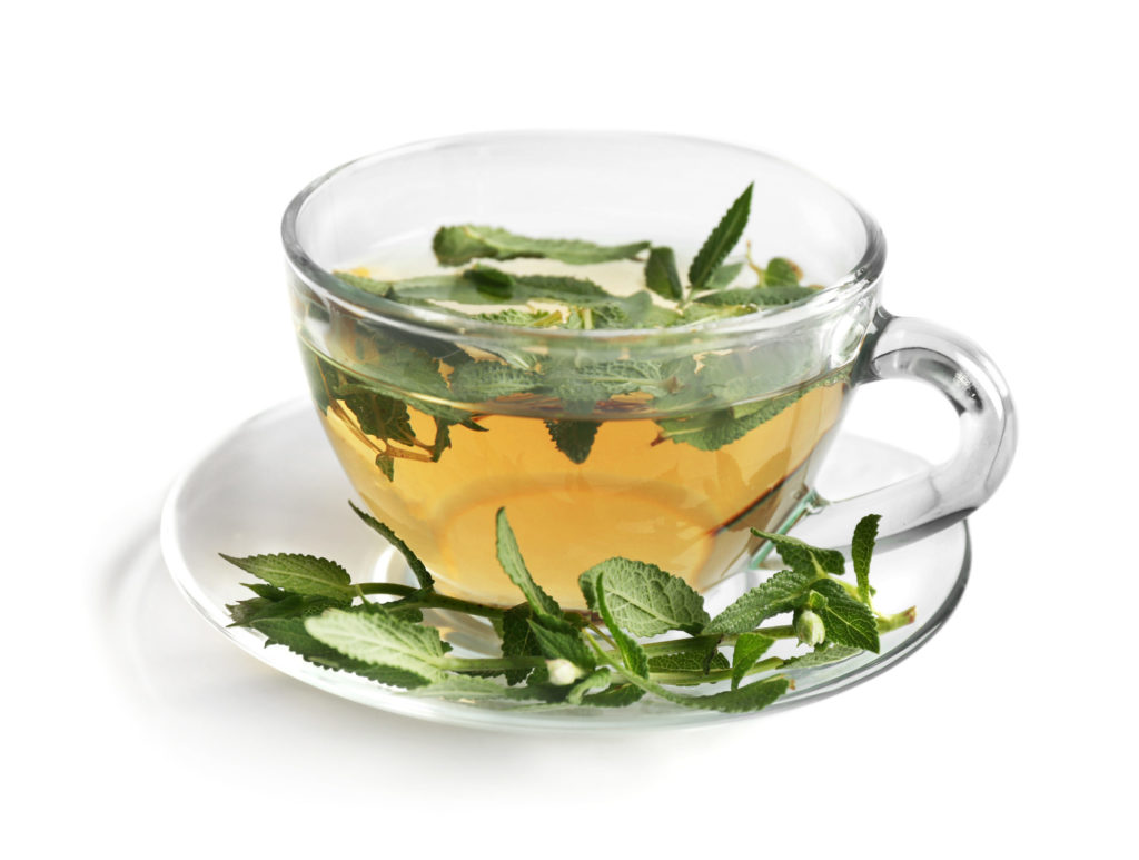 A cup of golden tea inside a clear glass teacup with sage leaves on the outside and inside served on a saucer in the traditional tea culture way.