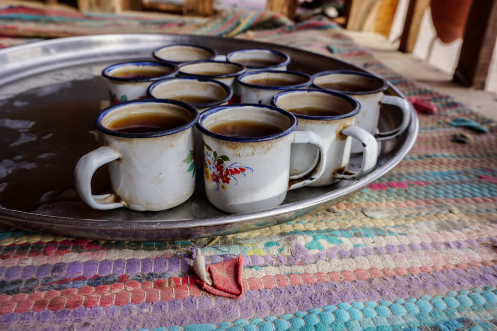 Multiple worn and weathered tea cups sit on a metal tray with Egyptian tea inside that is served according to traditional tea culture.