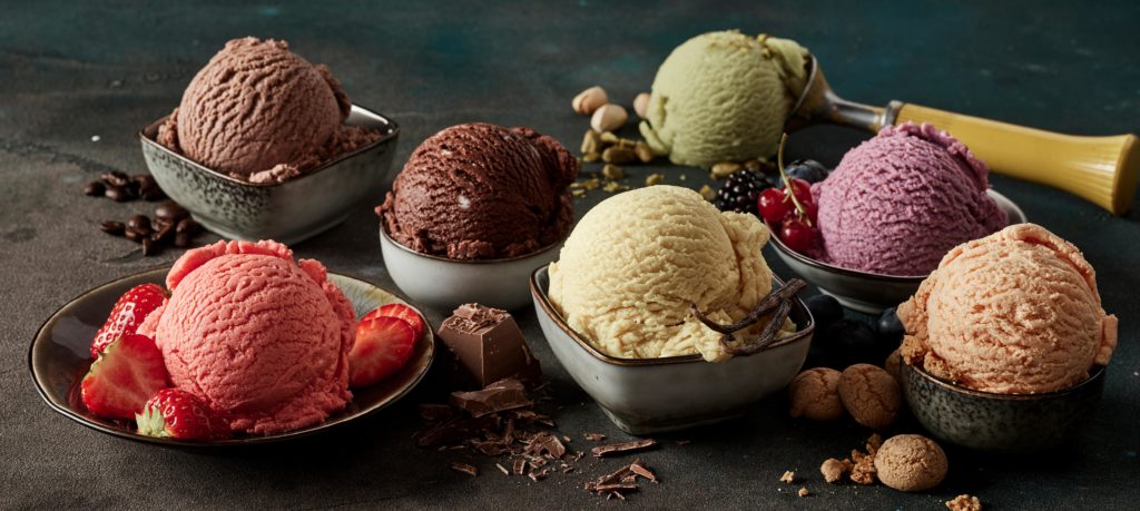 Multiple bowls of gourmet ice cream sit on a black table filled with colored desert flavors like berries, macaroons, coffee, pistachio, chocolate, and vanilla which was originated in China.