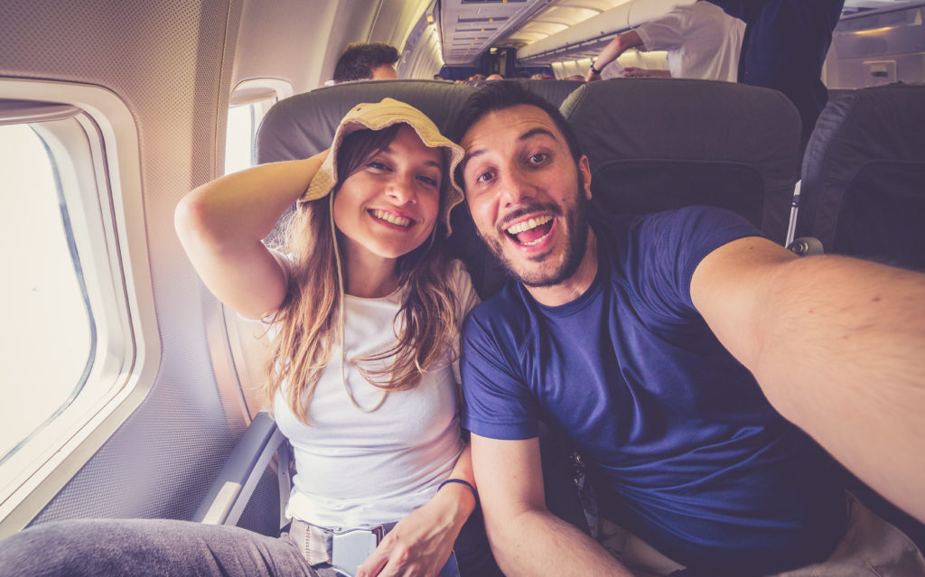 a couple takes a selfie while sitting on board a plane getting ready to depart for their vacation with Jaya Travel & Tours.