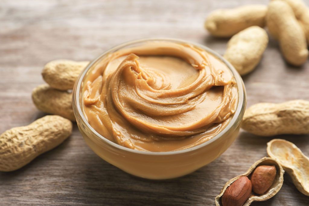 Glass bowl of peanut butter for snacking sitting on a wooden table with peanut snack food that was invented in Canada.