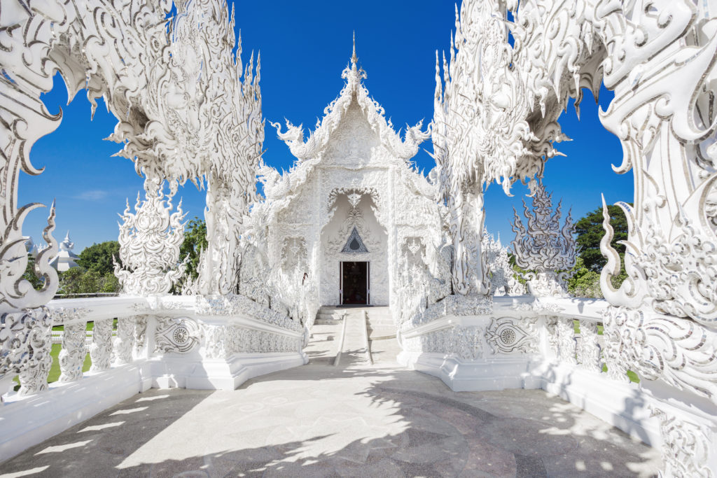 The view standing in front of Wat Rong Khun, aka The White Temple, in Chiang Rai, Thailand that is decorated with intricate mirror details and Buddhist teachings.