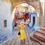 A young woman traveler in a yellow dress from Jaya Travel & Tours shopping the local stores in the medina of the blue city Chefchaouen in Morocco.
