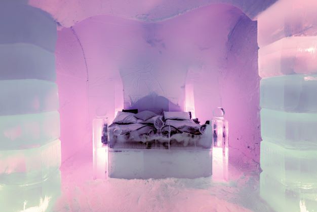 A picture looking into the Ice Hotel in Switzerland, where a bed carved from ice sits and purple highlights are casted along the snow. In this article, Jaya Travel & Tours recommends spending your spring break in Switzerland!