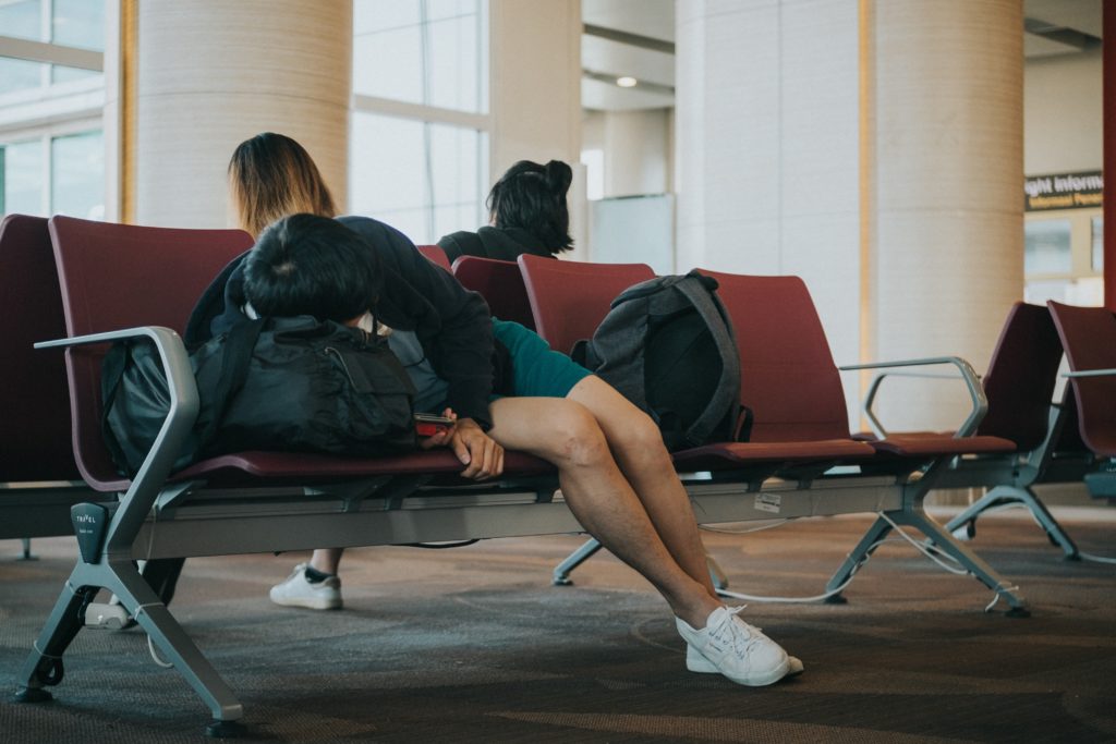 A male traveler sleeping on a chair in the airport after a long overseas flight. They're suffering from jet lag, which jaya travel & tours knows all of the tips to overcome jetlag.
