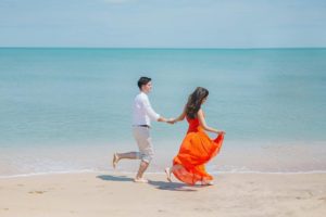 A young married couple hand in hand joyfully running on a sandy beach for a Valentine's Day Honeymoon destination with Jaya Travel & Tours.