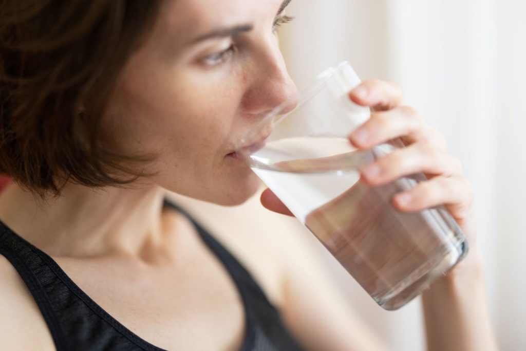 a woman drinking a large glass of water, trying to hydrate their body. This is a tip from Jaya Travel & Tours and their guide to overcoming jet lag.