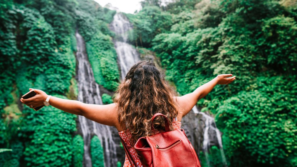 A young female traveler is on a hiking tour of waterfalls and enjoying the view of the waterfall. This is the featured image for Jaya Travel & Tours travel blog article, "Which Waterfall Should You Visit Quiz?"