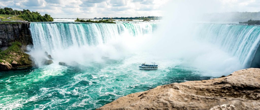 The featured image in the Jaya Travel & Tours article "Which Waterfall Should You Visit Quiz?" The image is a wide shot of Niagara Falls in America with a large tour boat in the water on a tour of the waterfalls.