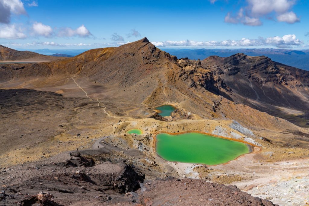 The Tongariro National Park in New Zealand, Australia is a unique landscape with rocky mountains and bright green lakes. This photo is featured in Jaya Travel & Tours blog, "On Location: The Lord of the Rings," which describes the real life filming locations of famous movies, with photo credit from IMDB.
