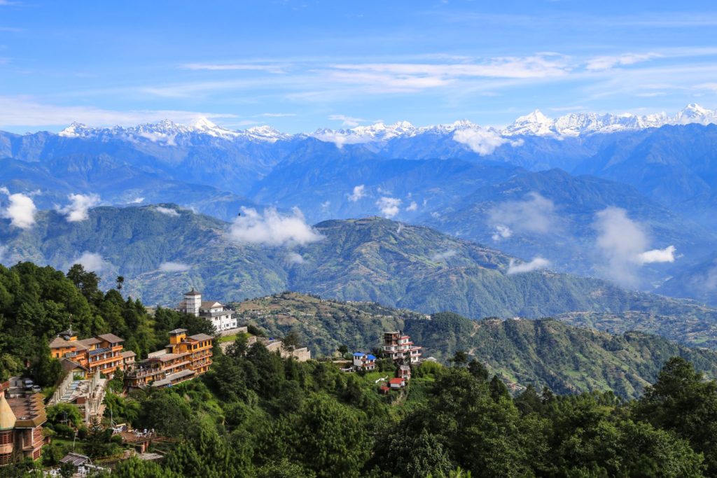 Jaya Travel & Tours features a beautiful image of Mount Everest in Nagarkot, Nepal on their weekly travel blog for vacation tips, interesting destinations, and travel quizzes. In the image, Mount Everest rises tall with with snow and clouds blanketing the top, and a small village built on top of a smaller, flatter mountain nearby.