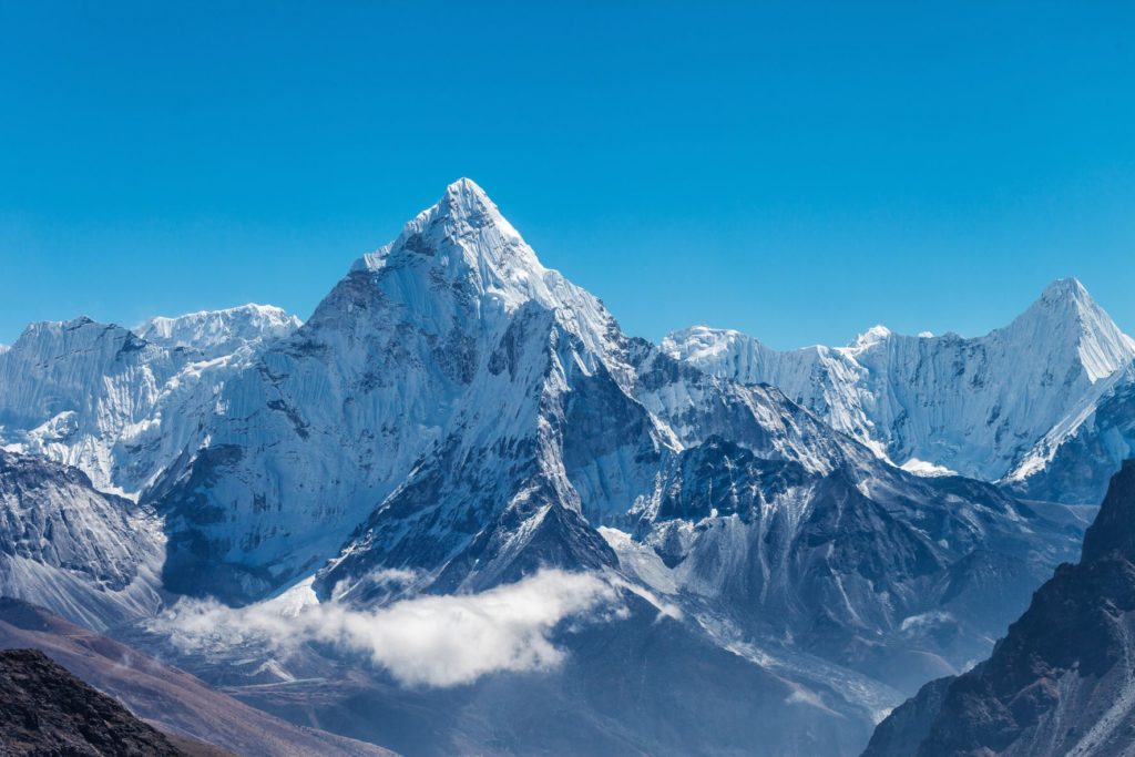 The Himalayan Mountains in Nepal, which is a top 10 destination of 2023 for Jaya, and is featured in the Jaya Travel & Tours blog about tours and popular spots in Nepal. An imposing, jagged mountain rises high above the clouds and is set against a clear blue sky, the perfect day for a tour of the vacation destination.