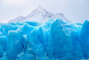 An image used in Jaya Travel & Tours travel quiz blog "Which Glacier Should You Visit Quiz?" A large glacier is set in front of a snowy white mountain, and the vibrant blue color of the ice is extremely noticeable.