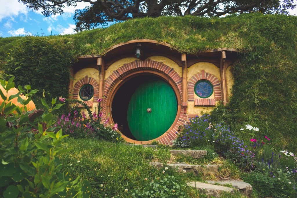 The featured image in Jaya Travel & Tours travel blog post "On Location: The Lord of the Rings" which lists the filming locations from Peter Jackson's popular movie trilogy, based on the iconic books from J. R. R. Tolkien. A tall, grassy hill is the walls of a Hobbit house in Hobbiton in New Zealand, Australia.