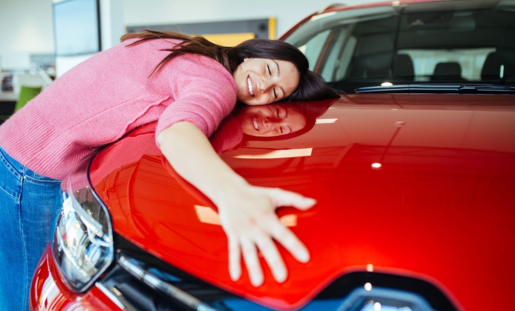 A young woman hugs the hood of a red rental car that she picked up at the airport for easy transfers on her vacation tours. In the Jaya Travel article "6 Reasons to Get Travel Insurance," we describe what travel insurance and trip protection can do to protect your vacation and your wallet.