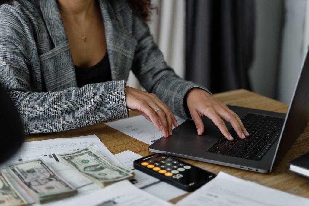 A young female in a suit types on her laptop with money, calculators, and papers scattered around while she tries to save money for vacation. In the Jaya Travel article "6 Reasons to Get Travel Insurance," we describe what travel insurance and trip protection can do to protect your vacation and your wallet.