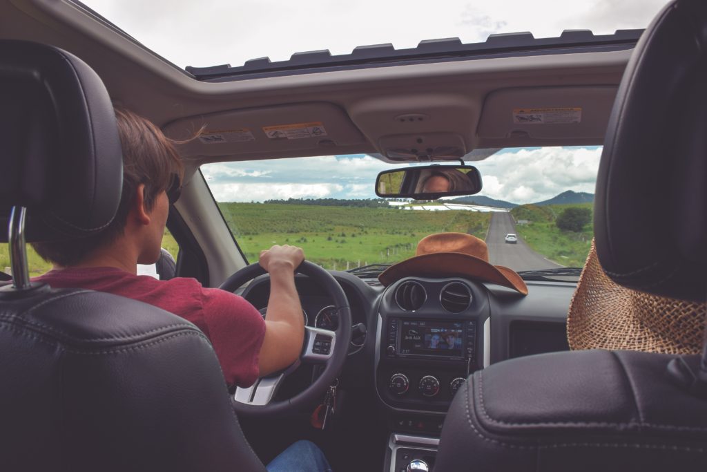 A photo taken from the backseat of a car of a couple driving on the highway together on a road trip. They are in a rental car with auto insurance purchased for their protection from Jaya. This image is featured in the Jaya Travel & Tours blog, "A United States Road Trip," which is a travel guide to the best road trips and driving the best highways in America.