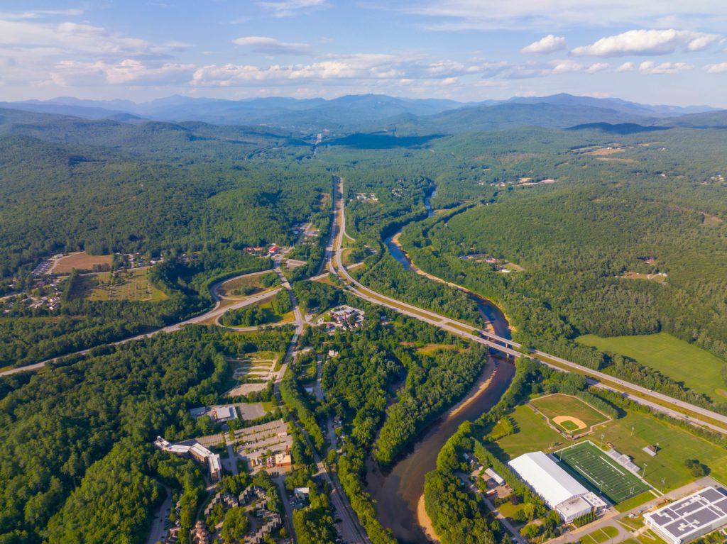 A landscape shot of the American highway system with multiple different highways and bridges and underpasses, set to a backdrop of the Outer Banks rivers and forests. This image is featured in the Jaya Travel & Tours blog, "A United States Road Trip," which is a travel guide to the best road trips and driving the best highways in America.