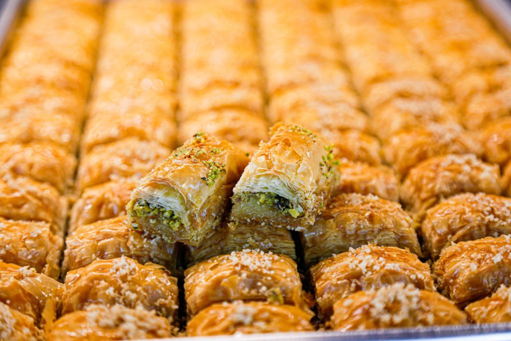 A large tray of the sweet and popular pastry baklava, which is a thin dough layered with pistachios and oil. This image is featured in the blog from Sky Bird Travel & Tours, "A Guide To Turkish Cuisine," which describes the types of food, drink, desserts, and dishes from Turkey.