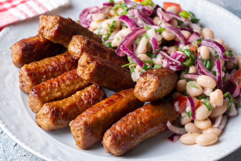 A plate of traditional Turkish food, which includes a large scoop of piyaz salad and inegol kofte, or Turkish tekirdag, meatballs from Antalya. This image is featured in the blog from Sky Bird Travel & Tours, "A Guide To Turkish Cuisine," which describes the types of food, drink, desserts, and dishes from Turkey.