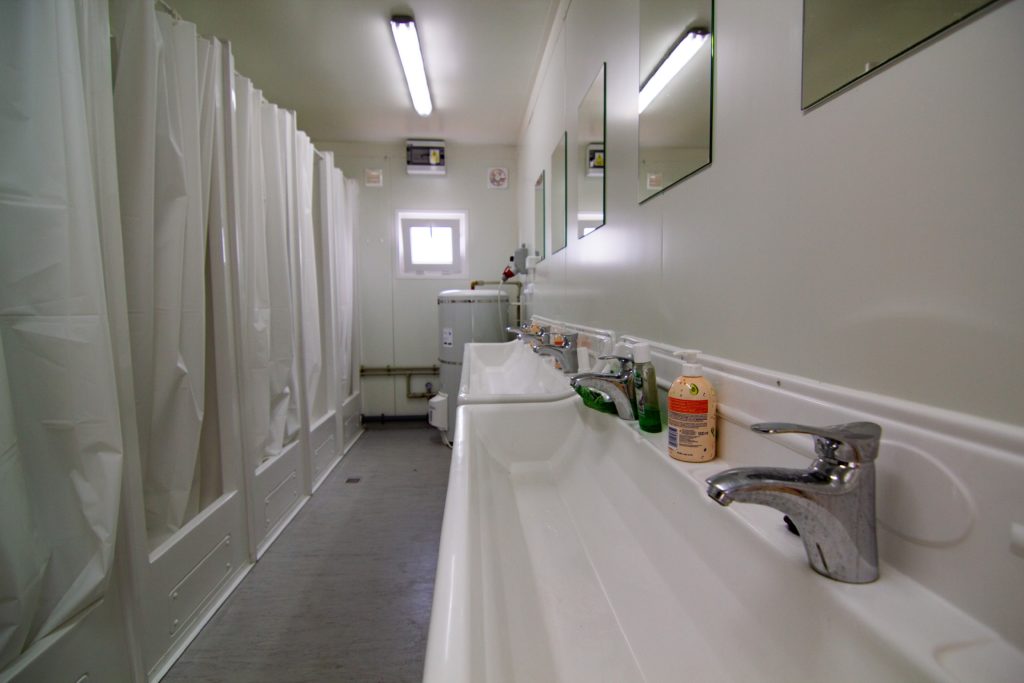 A very clean hostel bathroom with two large washing sinks and multiple small showers for guests to bathe on vacation for cheap. This image is featured in the Jaya Travel & Tours blog post, "Debunking 5 Myths About Hostels," which describes false lies about staying in a hostel on vacation and why they are incorrect.