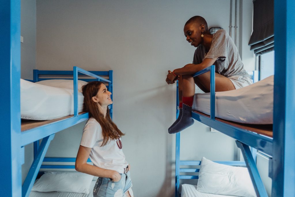 Two young women staying in a hostel, while they relax in the bedrooms on their bunkbeds. This image is featured in the Jaya Travel & Tours blog post, "Debunking 5 Myths About Hostels," which describes false lies about staying in a hostel on vacation and why they are incorrect.