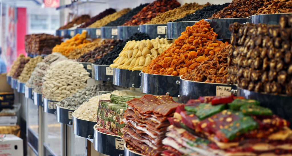 A close-up shot of a traditional market in Eastern Malatya Turkey, which is selling dried fruits, spices, fruits, nuts, cheeses, and fine grains. This image is featured in the blog from Sky Bird Travel & Tours, "A Guide To Turkish Cuisine," which describes the types of food, drink, desserts, and dishes from Turkey.