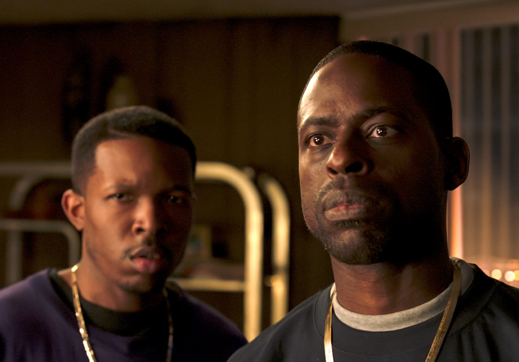 A still from the film, at Wheat Street Towers in Georgia, with two men looking at something outside of the frame with sad but serious faces. This image is featured in the Jaya Travel & Tours blog post, "On Location: Black Panther & Wakanda Forever," which lists the filming destinations of the popular marvel movie series.