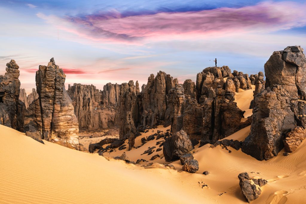 This image of a desert with rock formations and a vibrant sunset is featured in the Jaya Travel & Tours blog post "Africa Travel Guide"