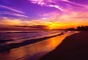 This image of purple, yellow, and orange sunset highlighting a beach with ocean waves is featured in the Jaya travel & Tours blog, "South America Travel Guide," which describes everything travelers should know about the destination.