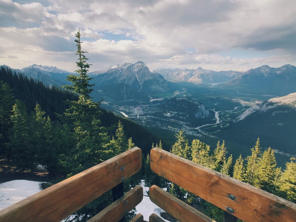 This image of a wilderness landscape in Canada with mountains in the distance and a river flowing in between a bank of trees is featured in the Jaya Travel & Tours blog, "North America Travel Guide," which describes everything about the destinations in North America.