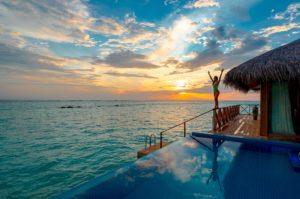 Featured in Unique Hotels Around the World by Jaya Travel & Tours, this image shows a woman at her overwater bungalow in Bora Bora and a beautiful sunset.