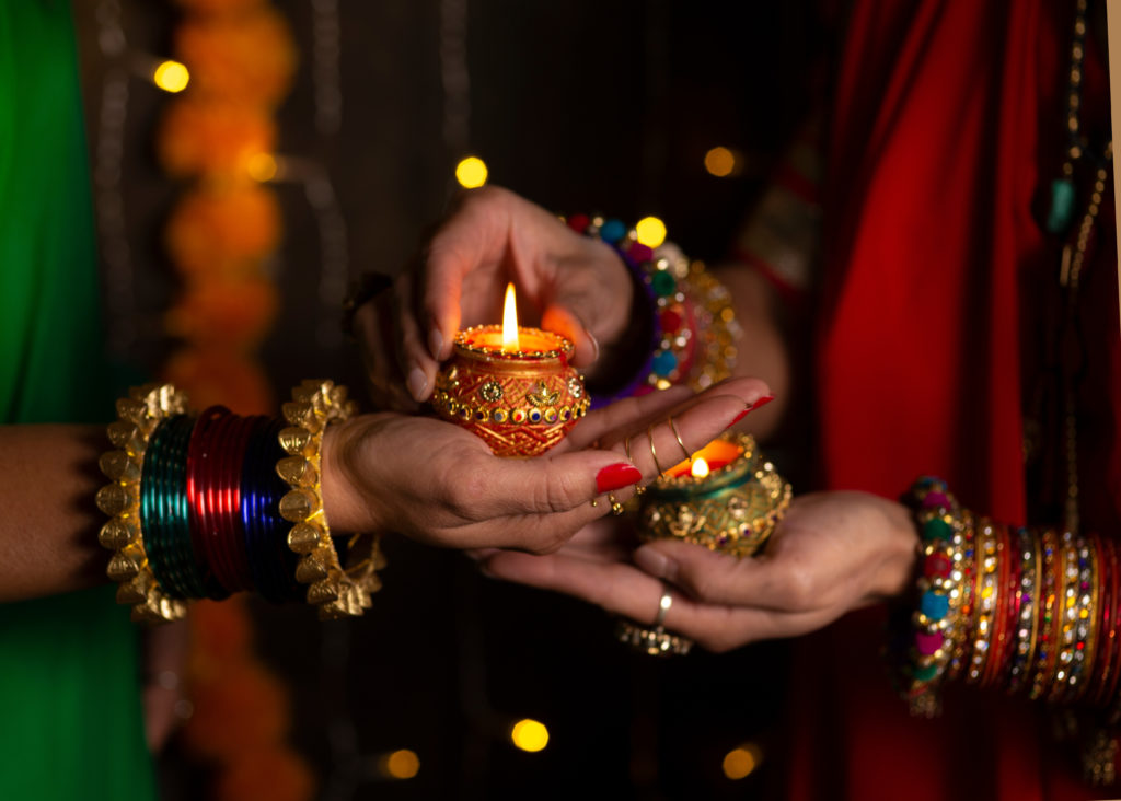 Featured in How to Celebrate Diwali by Jaya Travel & Tours, this image shows two women in Indian clothing lighting a diya lamp.