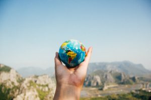 Featured in the Jaya Travel & Tours blog "Which Country To Visit Quiz," this image shows a hand holding a globe of the Earth in front of a mountain landscape.